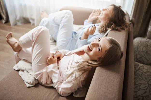 lazy-bones-doing-nothing-enjoying-leisure-together-upper-angle-shot-cute-women-sitting-sofa-nightwear-laughing-out-loud-talking-about-awkward-moments-office-spending-weekends_176420-8675