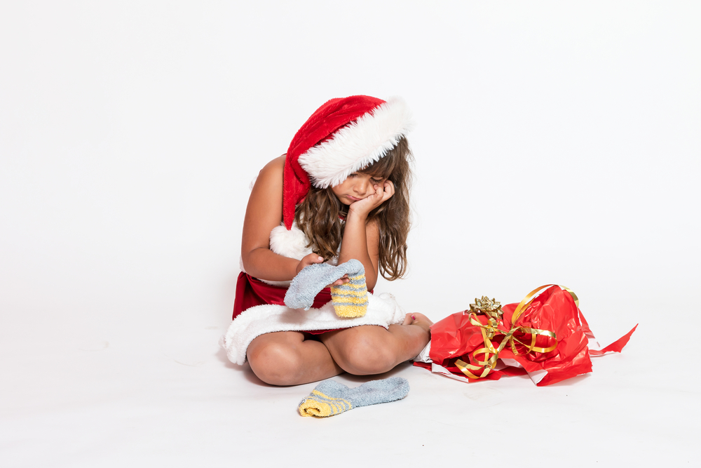 Sad girl in Santa Claus costume with inappropriate gift